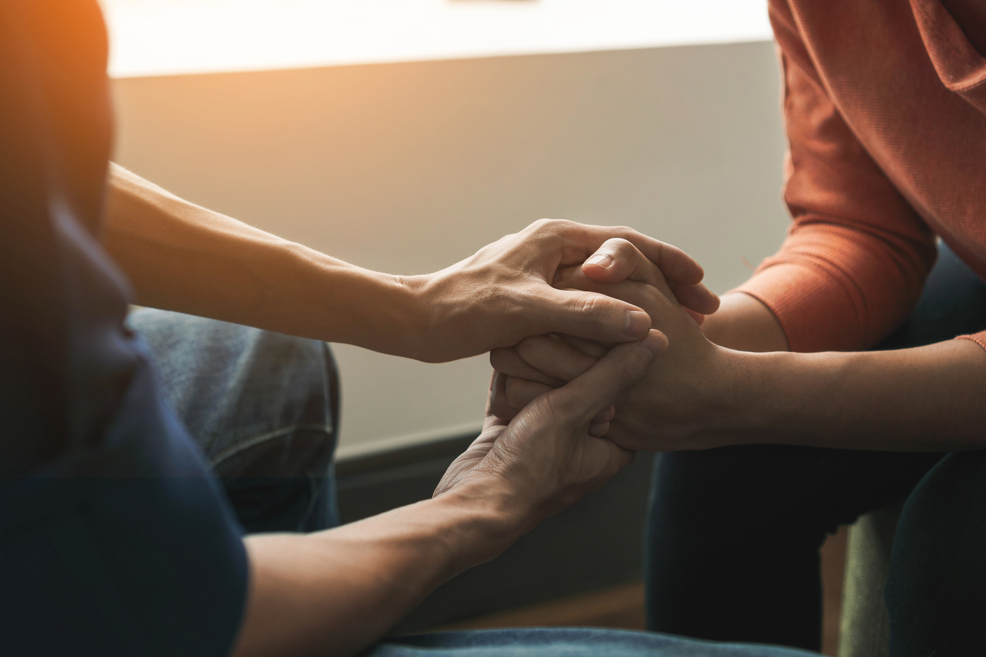 Two people sit close together in Beaverton, holding hands in a comforting gesture, with warm sunlight in the background, symbolizing support and empathy—much like the connection fostered through Ketamine Therapy.