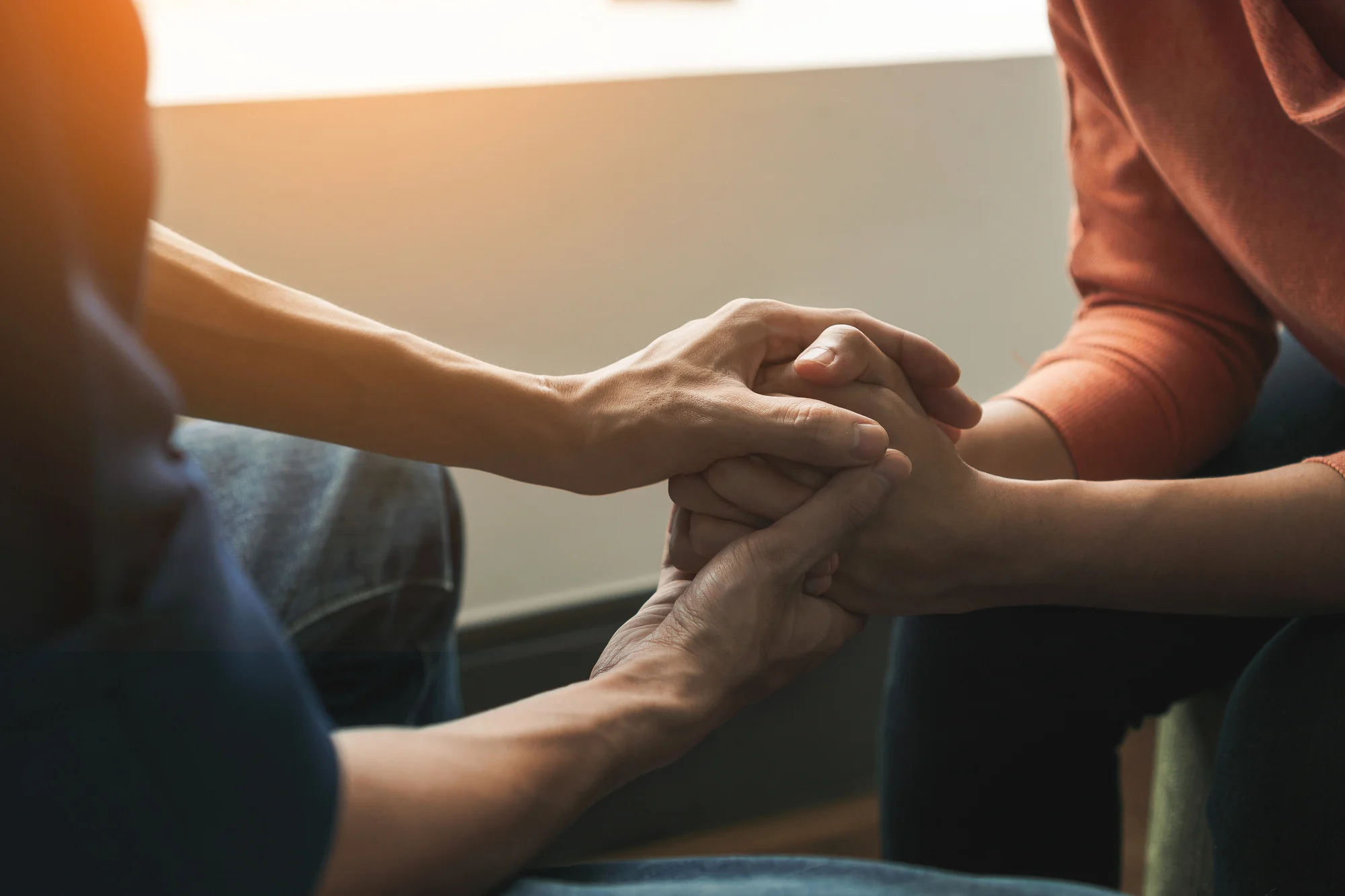 Two people sit close together in Beaverton, holding hands in a comforting gesture, with warm sunlight in the background, symbolizing support and empathy—much like the connection fostered through Ketamine Therapy.