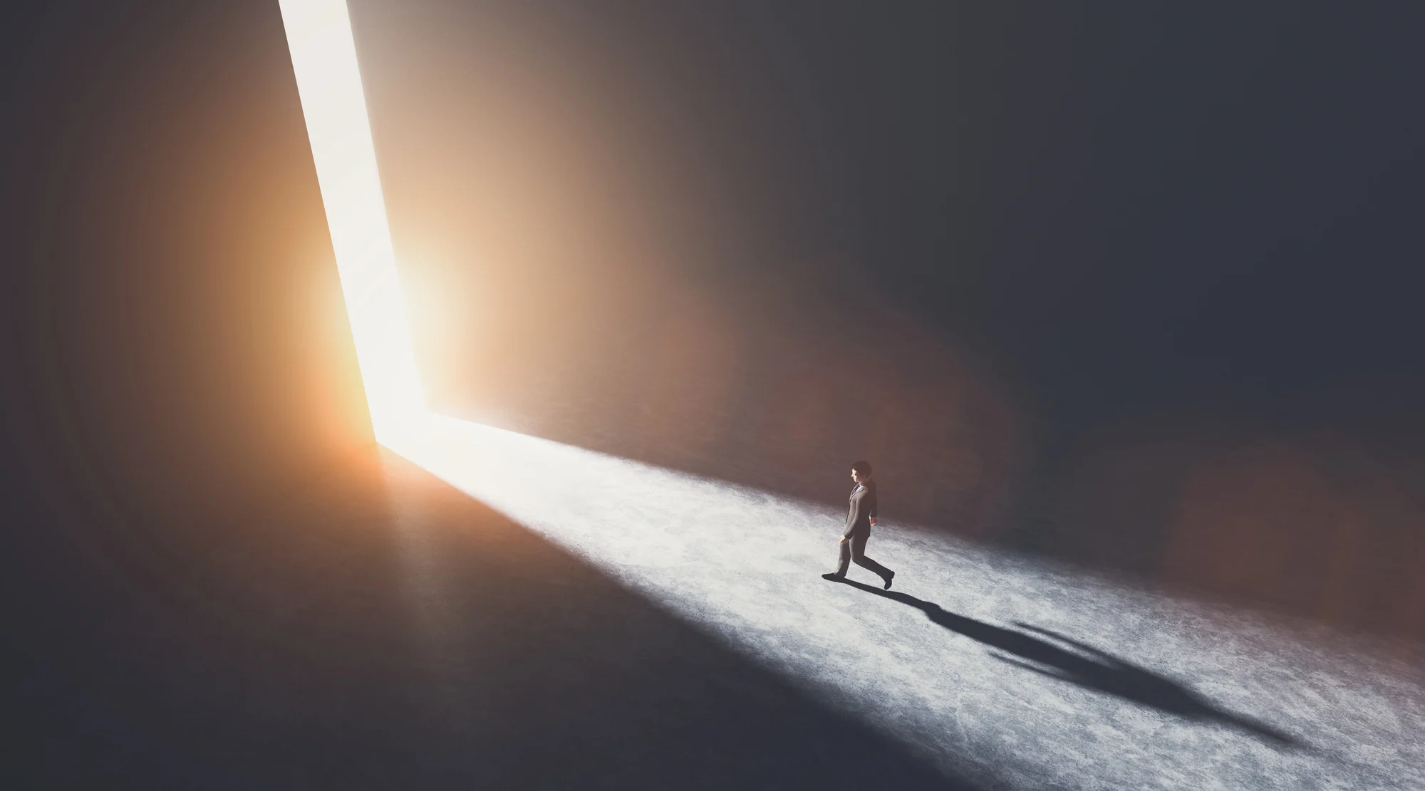 A person stands alone in a dark room in Beaverton, walking toward a large, bright doorway filled with sunlight—like emerging from ketamine therapy—casting a long shadow on the ground.