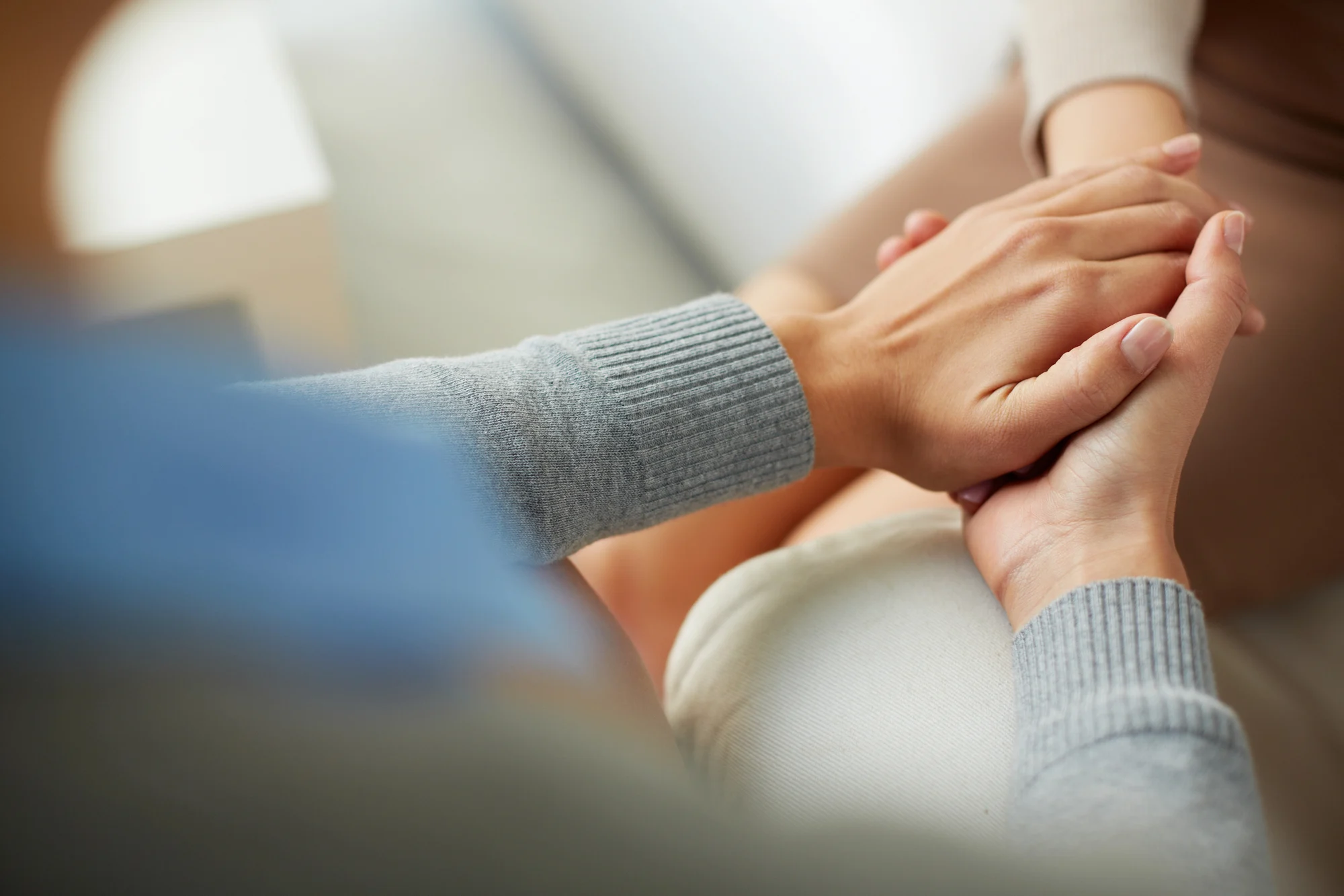 Close-up of one person gently holding another’s hands, offering comfort and support. Both are wearing long-sleeved clothing in a calm, intimate Sherwood setting—an atmosphere ideal for meaningful moments during Ketamine Therapy.