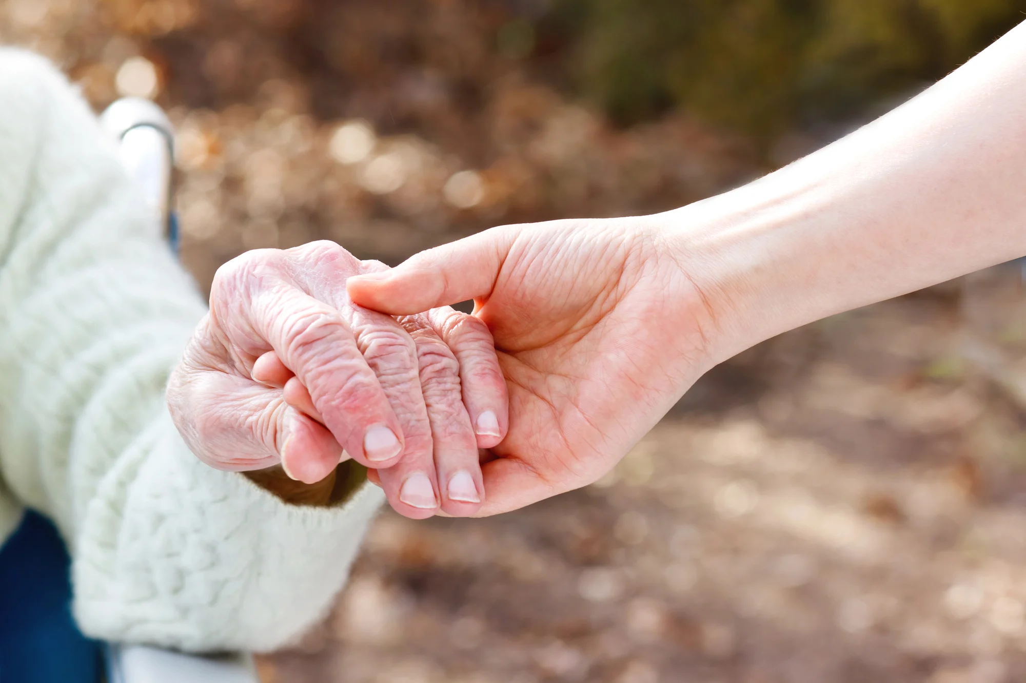 A younger person gently holds the hand of an elderly individual wearing a light-colored sweater, conveying care and support. The softly blurred background evokes warmth, similar to the compassionate environment found at Ketamine Therapy in Hillsboro.